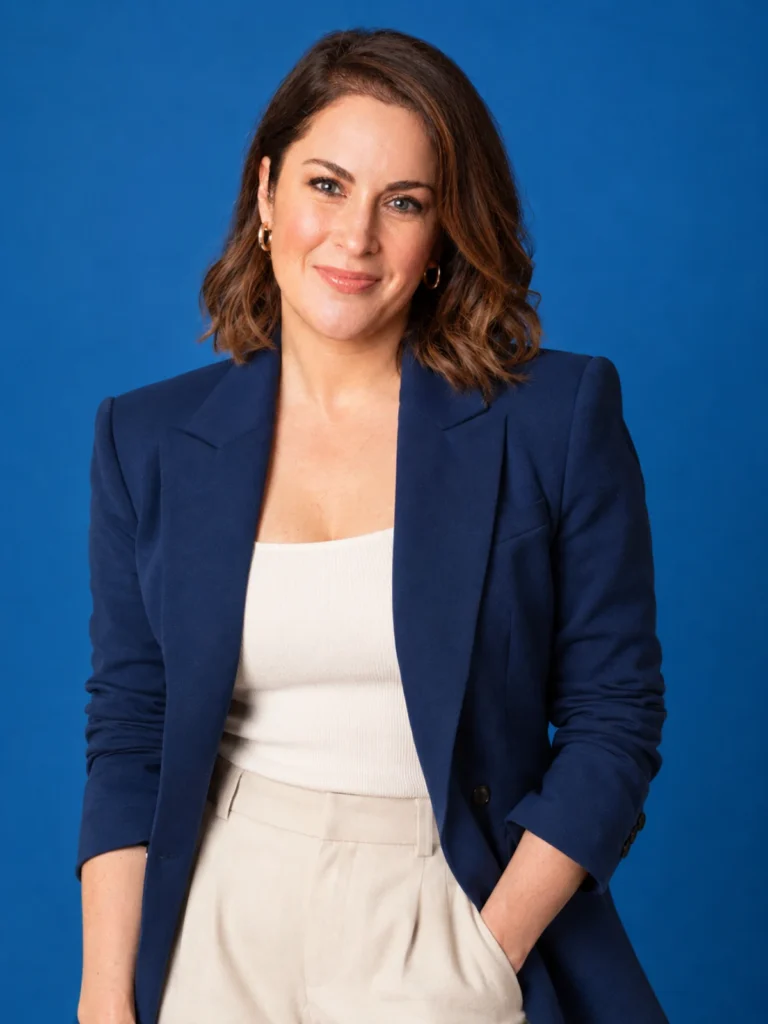 Melissa Stokes in a navy blazer and cream trousers posing against a blue studio background
