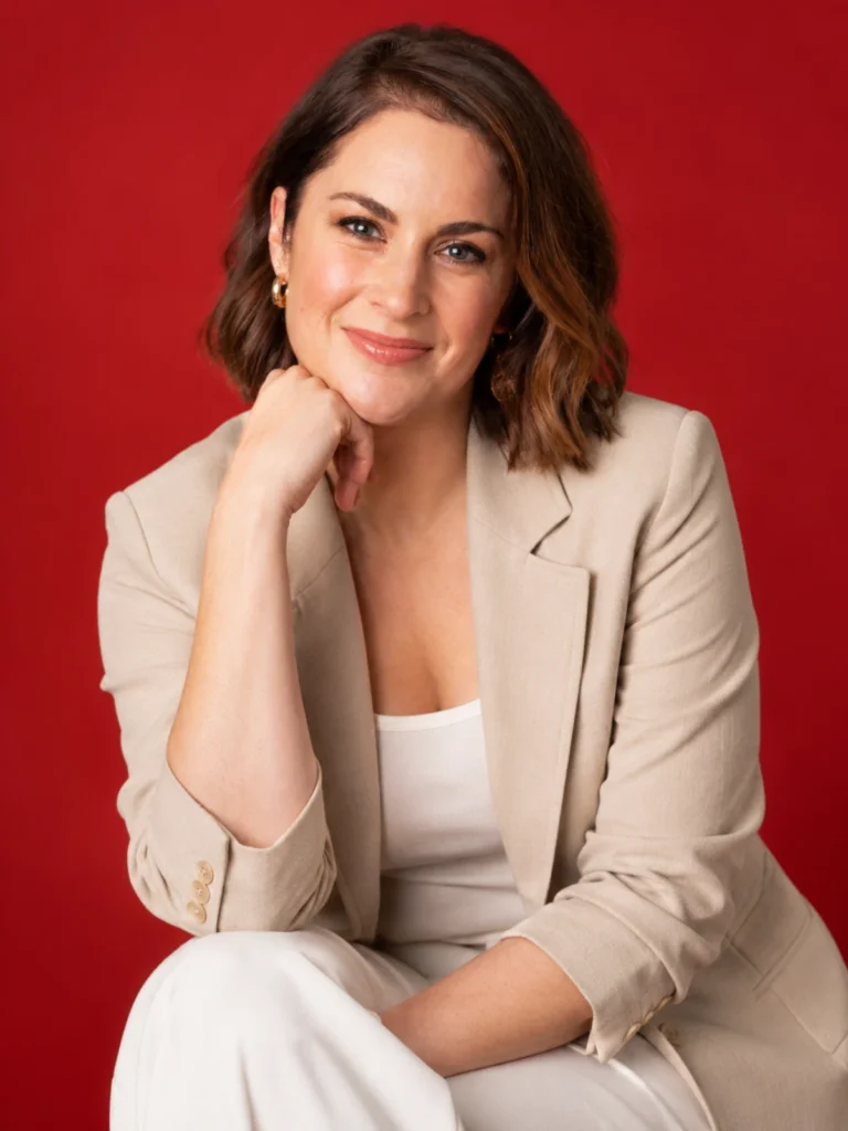 Melissa Stokes, 1News at Six presenter, smiling in a beige blazer against a red background